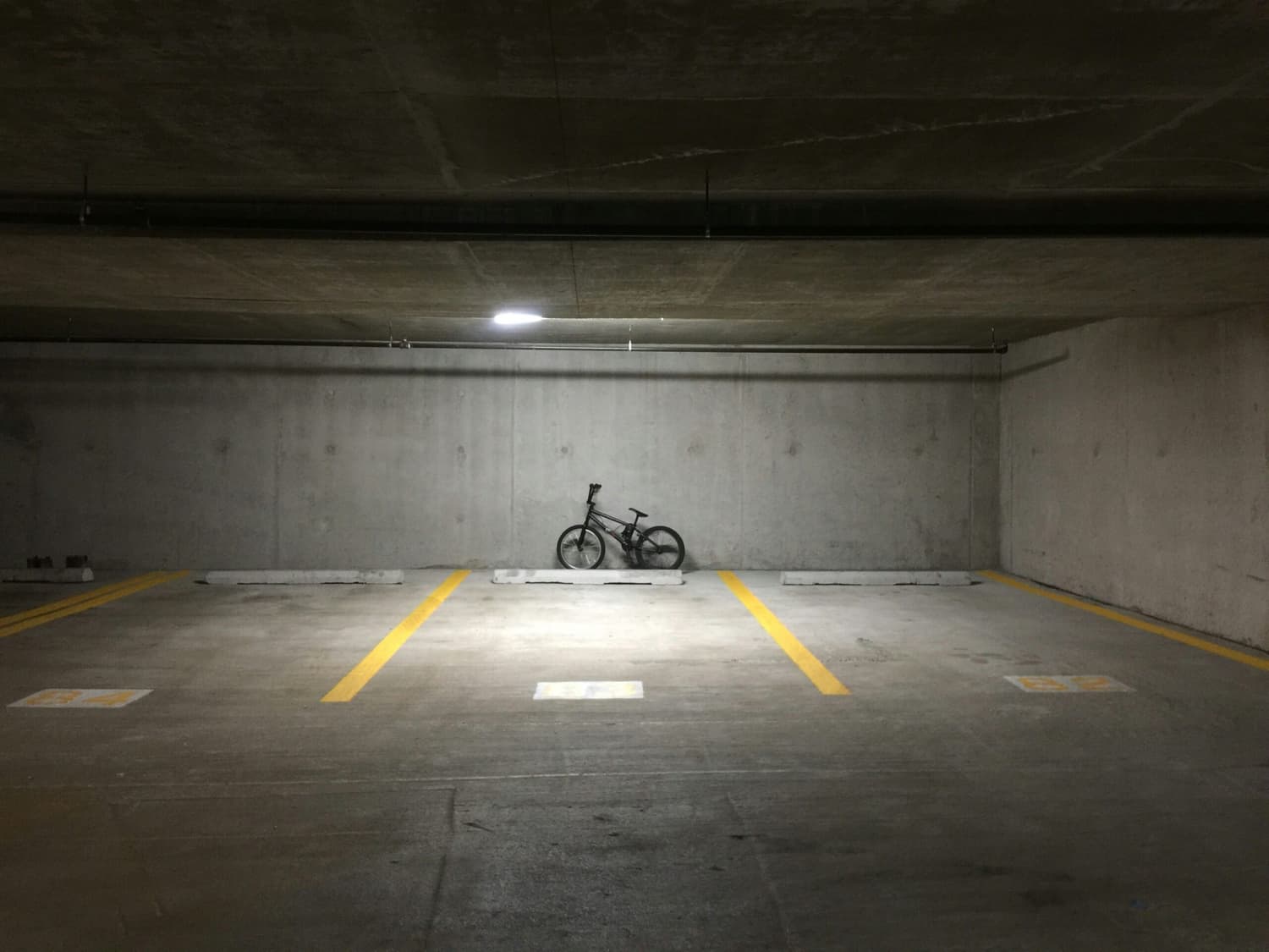 stacionamento subterrâneo vazio com uma única bicicleta estacionada em uma das vagas demarcadas, sob luz artificial. A imagem ilustra um ambiente típico de garagem residencial, ideal para representar temas relacionados ao aluguel de vaga de garagem em condomínio.